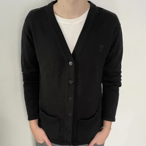 Svart kofta med knappar - Säljer en stilren svart kofta med knappar framtill. Koftan har långa ärmar och två fickor på framsidan. Perfekt för en avslappnad look.