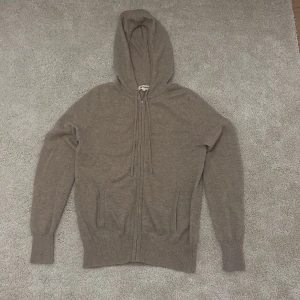 Biege hoodie från Soft Goat - Säljer en stilren biega hoodie från Soft Goat i kashmir. Tröjan har dragkedja och huva, samt snygga armbågslappar som ger en extra touch. Perfekt för kyliga dagar!