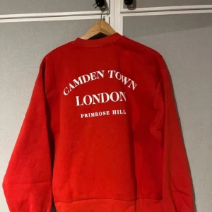 Röd sweatshirt från Gina Tricot - Säljer en röd sweatshirt från Gina Tricot med texten 'Camden Town London Primrose Hill' på baksidan. Tröjan har långa ärmar och en rund halsringning. Har inte kommit till användning och är som ny