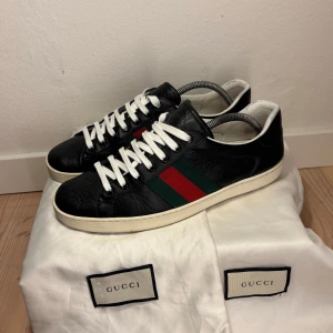 Gucci ace uk 7 - Snygga svarta sneakers från Gucci med klassiska gröna och röda ränder på sidan. Skorna har vita snören och en vit sula. Perfekta för en stilren look. Storlek 41 men passar storlek 42, dustbags kan medfölja vid kommunikation om det.