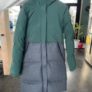 Grön och grå dunjacka från Sail Racing - Säljer en snygg grön och grå dunjacka från Sail Racing. Jackan har en lång design med huva och långa ärmar, perfekt för kyliga dagar. Den är stilren och funktionell, perfekt för vintern.
