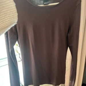 Brun långärmad tröja från Gina Tricot - Säljer en stilren brun långärmad tröja från Gina Tricot. Perfekt för en enkel och bekväm look. Tröjan har en rund halsringning och är gjord i ett mjukt material.