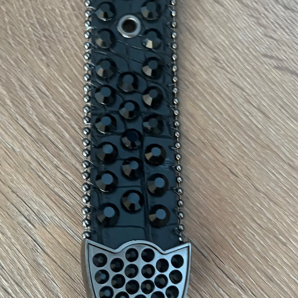 Snyggt svart bälte med glittriga detaljer och nitar. Bältet har en stor spänne dekorerad med svarta stenar och en cool design. Perfekt för att ge din outfit en extra edge.. Muu.