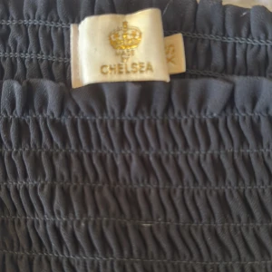 Svart kjol från Chelsea - Snygg svart kjol från Chelsea med en elastisk midja.. Kjolen har en kort längd och är gjord i ett lätt och luftigt material. Skriv för mer bilder