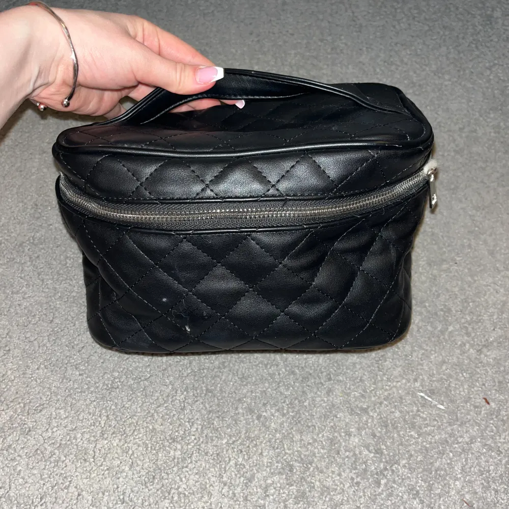 Snygg svart quiltad väska i syntetmaterial med praktisk dragkedja. Perfekt för att hålla ordning på dina saker. Den har ett handtag för enkel bärning. Använd ett par gånger som syns inuti. Laukut & Käsilaukut.