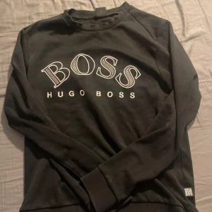 Svart sweatshirt från Hugo Boss - Snygg svart sweatshirt från Hugo Boss med stort BOSS-tryck på framsidan. Tröjan har långa ärmar och rund halsringning, perfekt för en stilren look. Passar bra till både jeans och chinos.