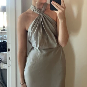 Grön balklänning med halterneck - Säljer min fina balklänning. Elegant grön/beige långklänning med halterneck-design. Klänningen har en draperad framsida och en smickrande passform. Älskar denna!! Nypris 1700 kr. Endast använd en gång och tvättad därefter.
