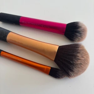 Sminkborstar från Real Techniques - Tre sminkborstar från Real Techniques i olika storlekar och färger. En rosa borste för rouge, en orange borste för puder och en mindre orange borste för foundation. Perfekta för att skapa en jämn och fin bas. Tvättas självklart innan det postas!