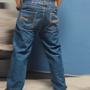 Blå jeans från Nudie Jeans - Säljer ett par klassiska blå jeans från Nudie Jeans. De har en snygg broderad detalj på bakfickan och knappar, tvärsnyggt högkvalite denimtyg. Håller länge.