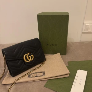 Svart quiltad axelväska från Gucci - Säljer en elegant svart quiltad axelväska från Gucci med guldfärgad kedja och GG-logga. Väskan har en stilren design och är perfekt för att ge en lyxig touch till din outfit. Kommer med originalförpackning och dustbag.