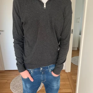 Zip up stickad - Säljer en stilren mörkgrå tröja med dragkedja vid halsen. Tröjan har långa ärmar och är perfekt för en avslappnad look. Passar bra till jeans eller chinos. Skick 8/10 