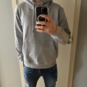 Grå hoodie från Jack & Jones - Säljer en stilren grå hoodie från Jack & Jones. Den har en klassisk design och en praktisk magficka. Perfekt för en avslappnad look. Passar till det mesta och är superbekväm! 🤍Helt ny aldrig använd därför är skicket 10/10😉