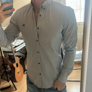 Ljusblå skjorta från Burberry Brit - Snygg ljusblå skjorta från Burberry Brit med klassisk krage och knappar framtill. Skjortan har en diskret logga broderad på bröstet och är perfekt för en stilren look. Passar bra till jeans eller chinos.