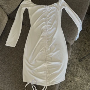 Vit ribbad klänning - Snygg vit ribbad klänning med långärmad design och offshoulder-stil. Klänningen har en smickrande passform med snörning framtill som ger en fin detalj. Perfekt för en stilren look.
