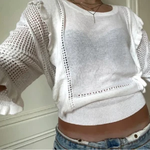 Vit stickad tröja med volangdetaljer - Säljer en vit stickad tröja med volangdetaljer och hålmönster. Tröjan har långa ärmar och en croppad passform, perfekt för en stilren look.