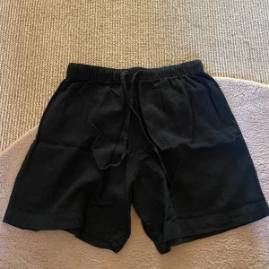 Svarta shorts - Säljer ett par svarta shorts från Monki i storlek XS. De är tillverkade i en blandning av linne och bomull, vilket gör dem både bekväma och stilrena. Shortsen har en elastisk midja med dragsko för justerbar passform.😻Perfekt till sommaren eller till vilka tillfällen som helst❤️