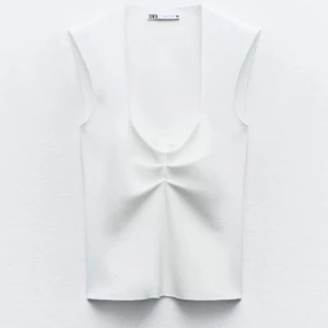 Vit ärmlös topp från Zara - Snygg vit ärmlös topp från Zara med djup urringning och stilren design. Perfekt för en minimalistisk look. Oanvänd.