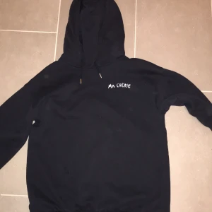 Mörkblå hoodie från Gina Tricot - Säljer en mörkblå hoodie från Gina Tricot med texten 'Ma Chérie' och hjärtmotiv på ryggen. Perfekt för en avslappnad stil. Hoodien har en klassisk design med huva och långa ärmar. Trendig och mysig😋