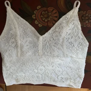 Vit spetslinne - Säljer ett vackert vitt spetslinne med smala axelband. Linnet har en elegant spetsdesign och är perfekt för varma dagar. Det är både stilrent och bekvämt.