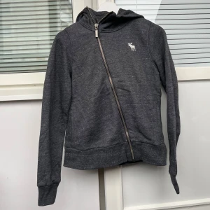 Assymetrisk Zip-Up - Cool och unik zip up ifrån Abercrombie & Fitch!💓Den har en dragkedja framtill och broderat ”Abercrombie” på luvan!😇💓I bra skick, inga defekter💓 