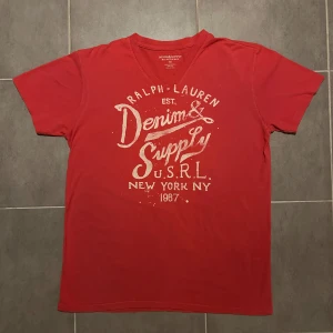 Ralph Lauren Denim and Supply T-shirt - (Nyskick) Säljer en röd/rosa t-shirt från Ralph Lauren med tryck framtill. T-shirten har en v-ringad hals och är kortärmad. Tillverkad i 100% bomull vilket gör den bekväm och lätt att bära.