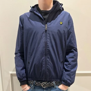 Blå Windbreaker - Tvär snygg Windbreaker från Lyle & Scott med dragkedja och huva. Perfekt nu till våran för de blåsiga dagarna. Köpt för omkring 700kr, men har blivit för liten därav jag säljer den. Storlek 14-15 år (XS). Bara att höra av dig vid frågor m.m. 