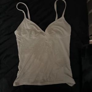 Vit linnetopp från Zara - Säljer en stilren vit linnetopp från Zara. Toppen har smala axelband och en enkel design som passar perfekt till sommaren. 