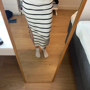 Vit och svart randig kjol - Snygg vit kjol med svarta ränder och en slits på sidan. Kjolen är ribbad och har en tight passform som framhäver figuren. Perfekt för en stilren look.