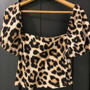 Leopardmönstrad topp från H&M - Säljer en trendig leopardmönstrad topp från H&M. Toppen har korta puffärmar och en ribbad struktur som ger en snygg look. Perfekt för att sticka ut med ett djärvt mönster.