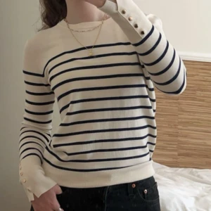 Randig tröja med knappar - Snygg randig tröja från Zara i vitt och blått med långa ärmar och dekorativa knappar vid ärmsluten. Perfekt för en stilren och avslappnad look.