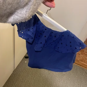 Blå offshoulder topp - Snygg blå offshoulder topp med volangdetaljer. Perfekt för sommarens varma dagar. Toppen har ett vackert broderat mönster på volangen som ger en extra touch.