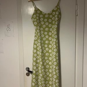 Grön blommig klänning från Glamorous Care - Säljer en söt grön klänning med vita blommor från Glamorous Care. Klänningen har smala axelband och en lång, elegant passform! 