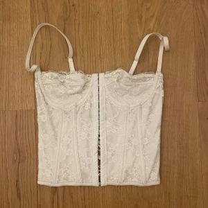 Vit spetskorsett -  vit korsett med spetsdetaljer och justerbara axelband. 