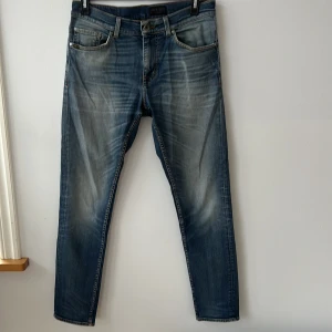 Blå jeans från Tiger of Sweden - Snygga blå jeans från Tiger of Sweden med en klassisk tvätt och lätt slitna detaljer. De har en normal passform och är perfekta för en avslappnad stil. Jeansen har fem fickor och stängs med dragkedja och knapp.