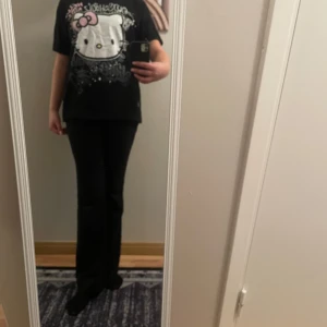 Svart Hello Kitty t-shirt - Cool svart t-shirt med stort Hello Kitty-tryck i vitt och rosa. Från new YORKER Texten 'Old School' och 'Hello Kitty' ger en retro känsla. Perfekt för dig som älskar unika och lekfulla plagg!
