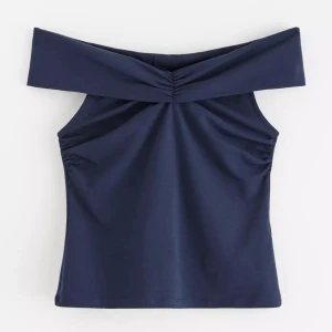 Mörkblå offshoulder topp från Holly & Whyte - Snygg mörkblå offshoulder topp från Holly & Whyte. Tillverkad i en återvunnen bomullsblandning, perfekt för en stilren look. Toppen har en elegant drapering vid axlarna och en figurnära passform. Aldrig använd med prislappen kvar