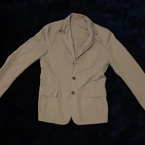 Beige kavaj från Moncler - Snygg beige kavaj från Moncler med klassisk design. Den har en dragkedja och knappar på framsidan. 