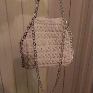 Vit virkad handväska med kedja - Säljer en unik vit virkad handväska med en stilren kedja. Perfekt för att ge din outfit en personlig touch. Väskan är handgjord och har en mjuk struktur.