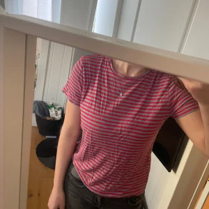 Randig t-shirt från NA-KD - Säljer en randig t-shirt från NA-KD i rött och grått. Den har korta ärmar och en klassisk rund halsringning. Perfekt för en avslappnad stil🥰använd 2 ggr. Hör av dig vid intresse!✨