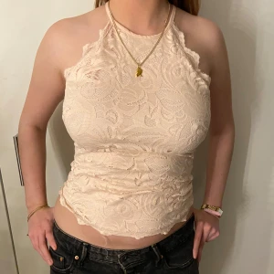 Rosa spetslinne - Säljer ett snyggt spetslinne med öppen rygg och knytning i nacken. Toppen är ärmlös och har ett vackert blommigt mönster. Perfekt för en somrig look!