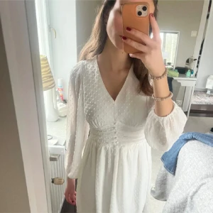 Vit kortklänning med prickar - Säljer en söt vit kortklänning med diskreta prickar och v-ringad hals. Klänningen har långa ärmar och en smickrande passform i midjan. Perfekt för sommarens alla tillfällen!