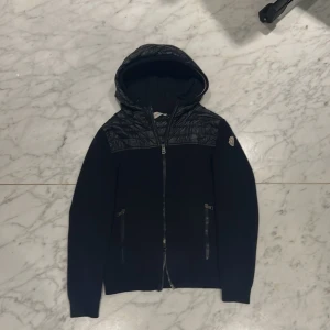 Mörkblå cardigan från Moncler - Snygg mörkblå jacka från Moncler med quiltade detaljer och huva. Jackan har dubbla dragkedja framtill och två praktiska fickor med dragkedjor. Perfekt för kyligare dagar med sin stilrena design och varma material. Säljer på grund av att jag börjar växa ut den. Pris diskuterbart vid snabb affär. Kontakta för frågor 