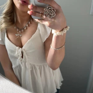 Vit blus med volangdetaljer - Charmig vit blus med volangdetaljer och knytning framtill. Den har korta ärmar och en luftig passform, perfekt för varmare dagar. Blusen är tillverkad i ett lätt och bekvämt material.