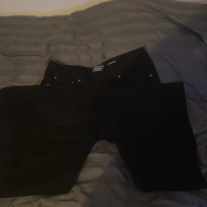 Svarta byxor från Dressmann - Snygga svarta byxor från Dressmann i regular fit. Perfekta för en stilren look. Byxorna har en klassisk design med knappar och dragkedja framtill.                PRIS KAN DISKUTERAS 