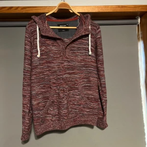 Varm kofta med luva - Säljer en snygg kofta i storlek M. Tröjan har en bekväm passform med långa ärmar och en praktisk känguruficka framtill. Den har en justerbar huva med vita snören. Perfekt för kyliga dagar!