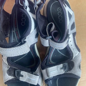 Grå och svarta sandaler från Ecco - Säljer ett par bekväma grå och svarta sandaler från Ecco med justerbara remmar och robust sula. Perfekta för sommarens äventyr. Sandalerna har en sportig design med röda detaljer på sulan.
