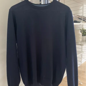 Mörkblå merinullströja från Coney Island - Säljer en stilren mörkblå merinullströja från Coney Island i storle. Tröjan har en klassisk rund hals och långa ärmar, perfekt för kyligare dagar. Ett måste i garderoben för den som gillar enkel och tidlös design. Hör av er vid frågor!