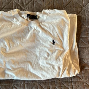 Vit t-shirt från Polo Ralph Lauren - Säljer en klassisk vit t-shirt från Polo Ralph Lauren med det ikoniska broderade logotypen på bröstet. Perfekt för en stilren och avslappnad look. T-shirten är kortärmad och tillverkad i mjuk bomull.