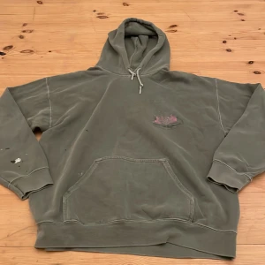 Grön hoodie med tryck - Säljer en grön hoodie med ett coolt tryck på baksidan. Hoodien har en känguruficka och långa ärmar. Perfekt för en avslappnad stil. Hopdien har en större färg fläck på baksidan av högra armen och men mindre vid högra hörnet av fickan. Den är ifrån Urban outfitters orginaltrogen pris: 400