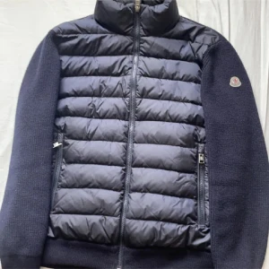 Moncler cardigan  - Säljer en snygg mörkblå cardigan från Moncler. Jackan har en dragkedja framtill och långa ärmar. Den är perfekt för kyligare dagar med sin kombination av quiltat material och stickade detaljer på ärmarna. Äkta finns bevis. Köpt för ca 9000kr. Tar bud samt byten.